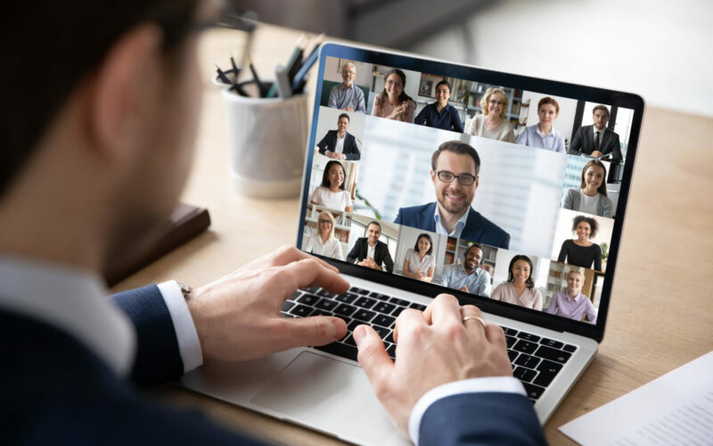 Rear view of businessman speak on web conference with diverse colleagues using laptop Webcam, male employee talk on video call with multiracial coworkers have online meeting briefing from home