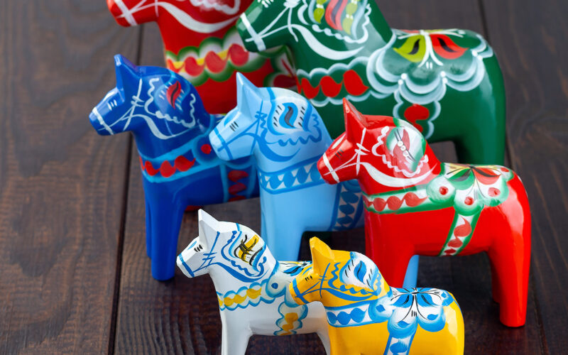 Swedish traditional souvenir wooden dala horses, hand craft made and painted, different colors and sizes, on a wooden background,  horizontal, copy space