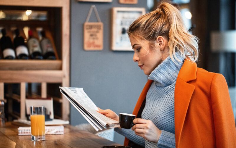 Female freelancer relaxing on coffee break and reading newspaper in cafeteria.